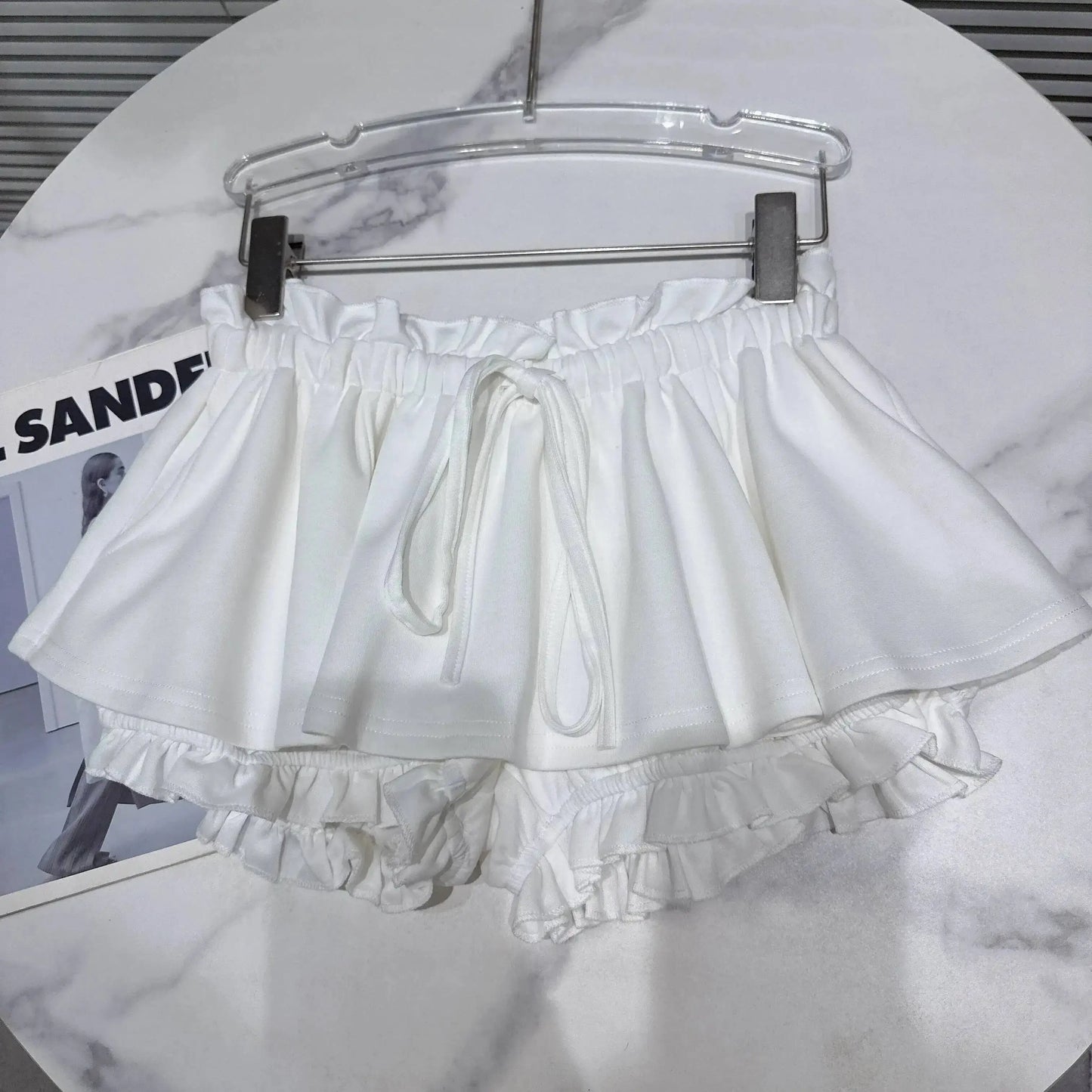 Layered Ruffle Drawstring Mini Skort in white hanging on a rack, showcasing its playful and feminine design.