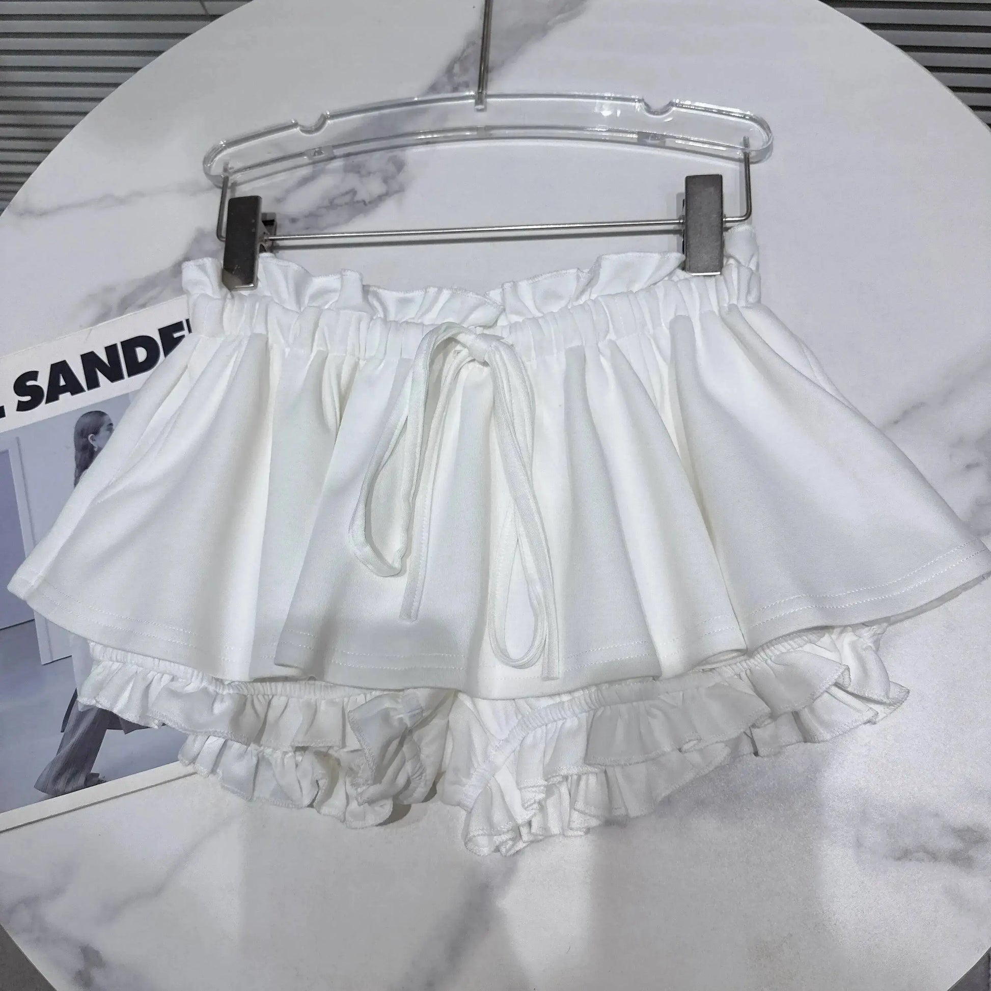 Layered Ruffle Drawstring Mini Skort in white hanging on a rack, showcasing its playful and feminine design.