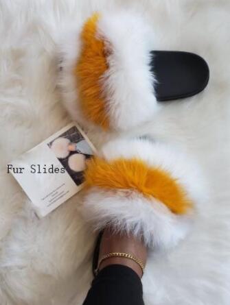 Plush faux fur slides with white and orange fur, resting on a cozy fur surface next to a card.