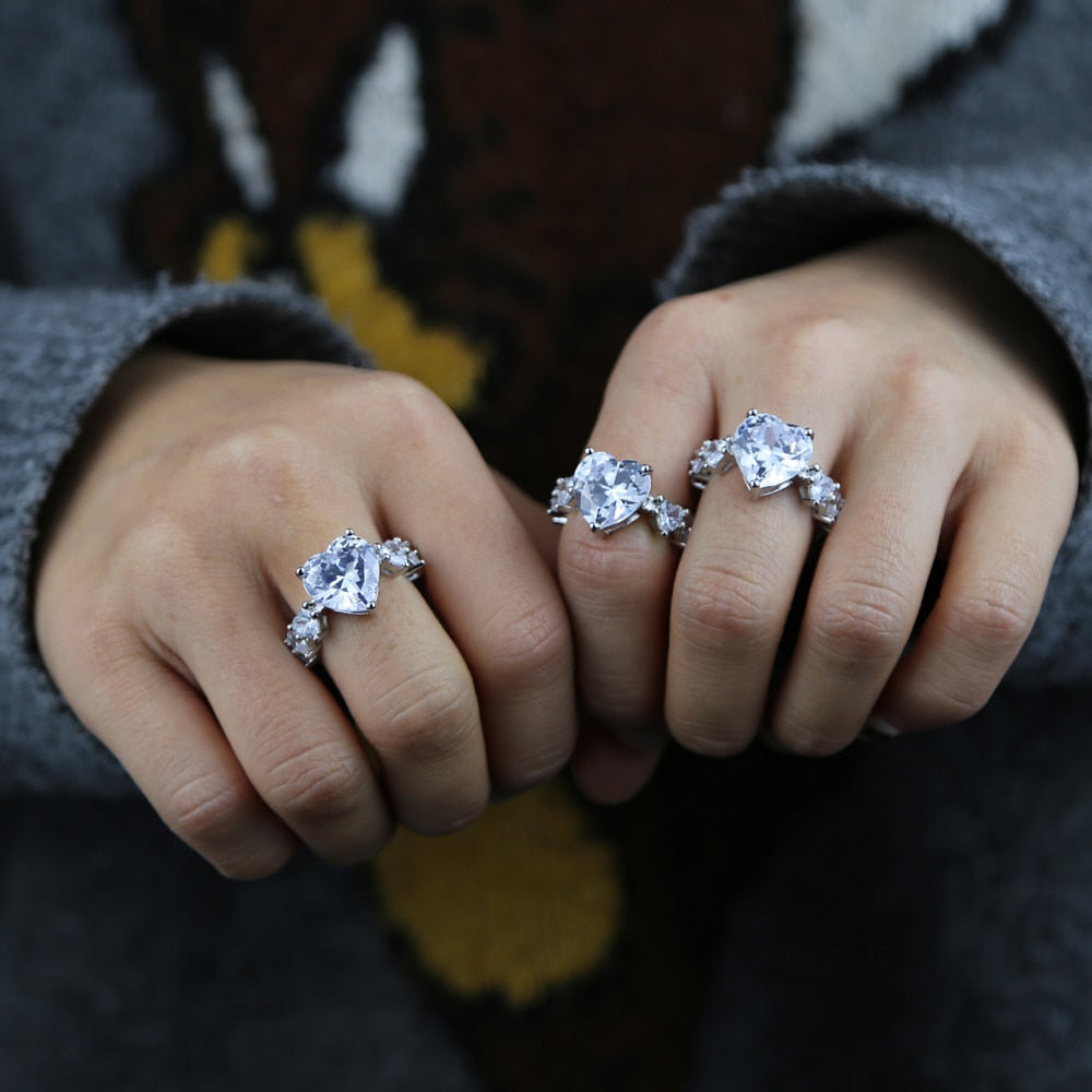 Two hands displaying multiple cubic zirconia heart rings featuring prong settings and elegant designs.